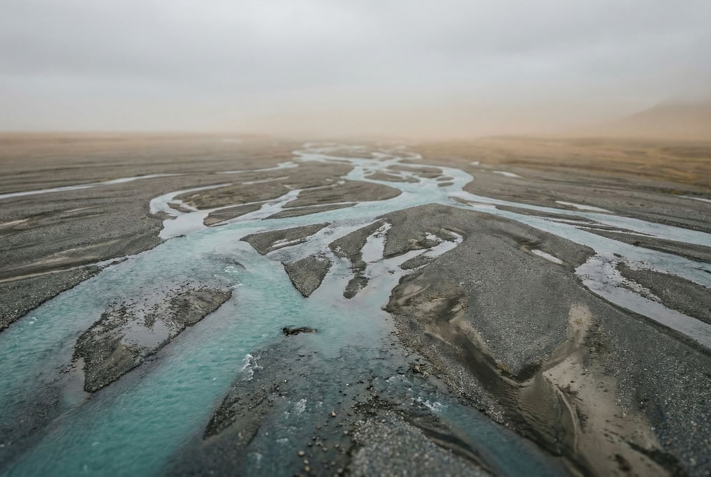 Turquoise glacial meltwater river braiding across a gray gravel plain, seen from above (ce60hgcd)