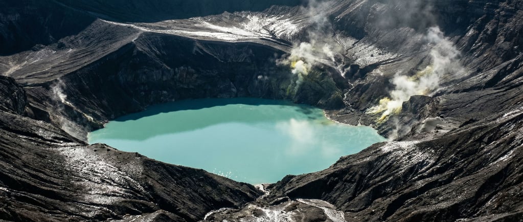 A volcanic caldera lake, perfectly still turquoise water surrounded by dark ash-covered slopes and w (aqxtiuh6)