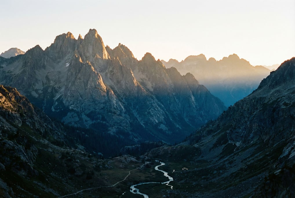 A jagged granite ridge at dawn, the first rays of sunlight hitting only the highest peaks while vall (lwxj5dm)