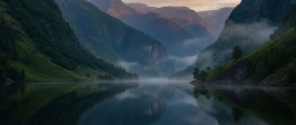 Fjord at dawn, dark mirror-still water stretching between steep green mountains disappearing into mi (drd3rg9c)