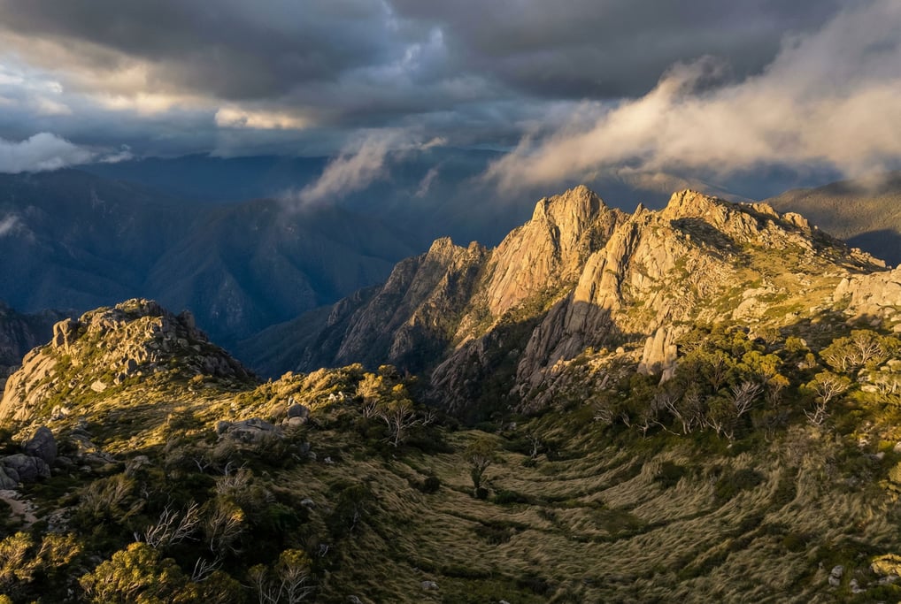 A jagged granite ridge at dawn, the first rays of sunlight hitting only the highest peaks while vall (ajxnzjri)