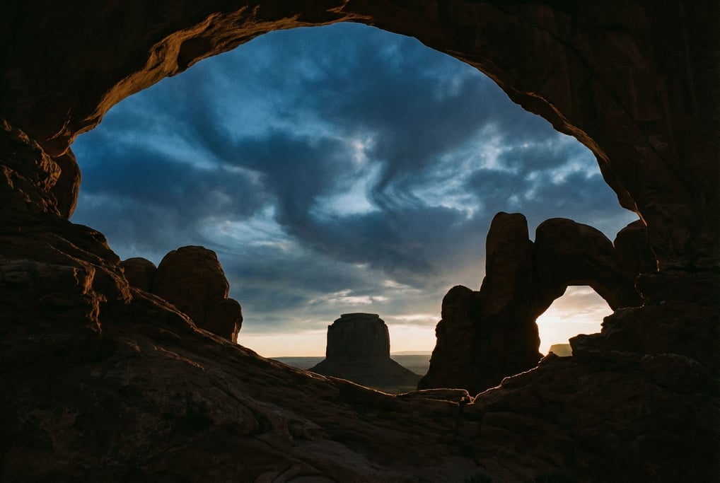Wind-carved sandstone arches framing a distant mesa, warm red rock against blue sky (tz24rvhg)