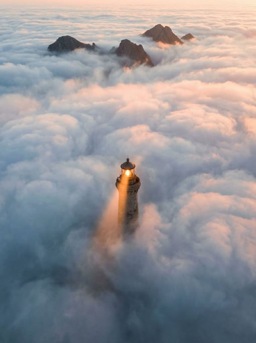 A lighthouse standing in the middle of a cloud sea viewed from above