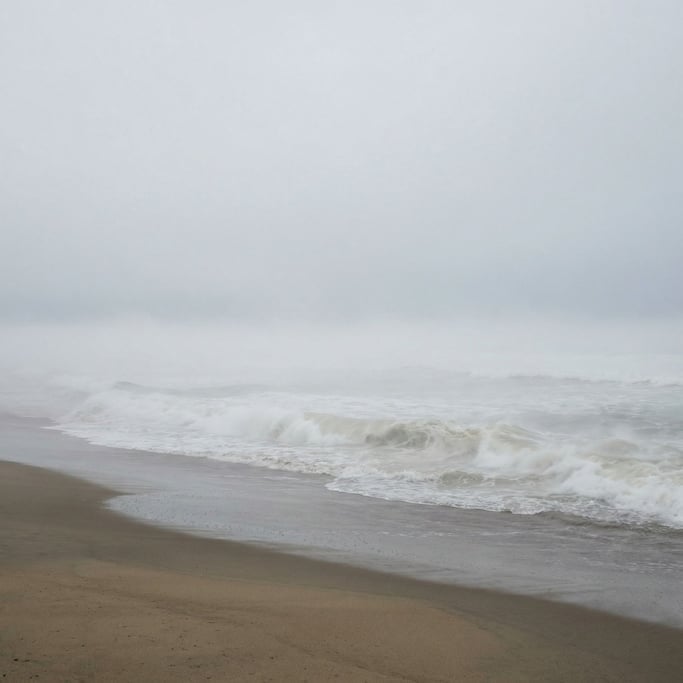 A beach where the incoming tide brings not water but thick fog that flows in wave-like surges up the sand