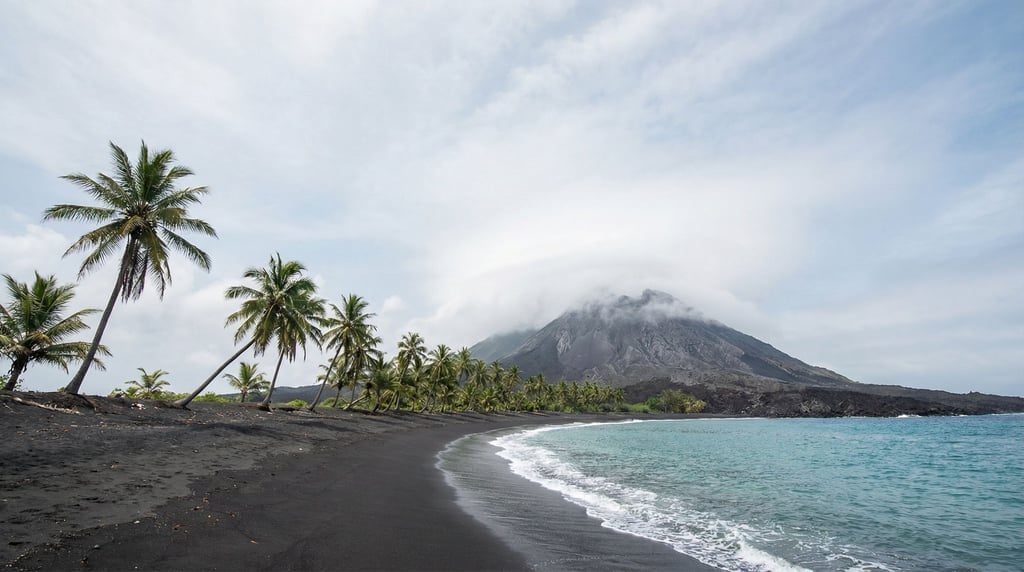 A tropical volcanic island beach with jet-black sand meeting turquoise water