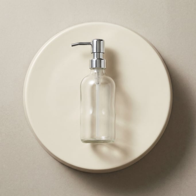 Pump dispenser bottle in clear glass, single on a pedestal