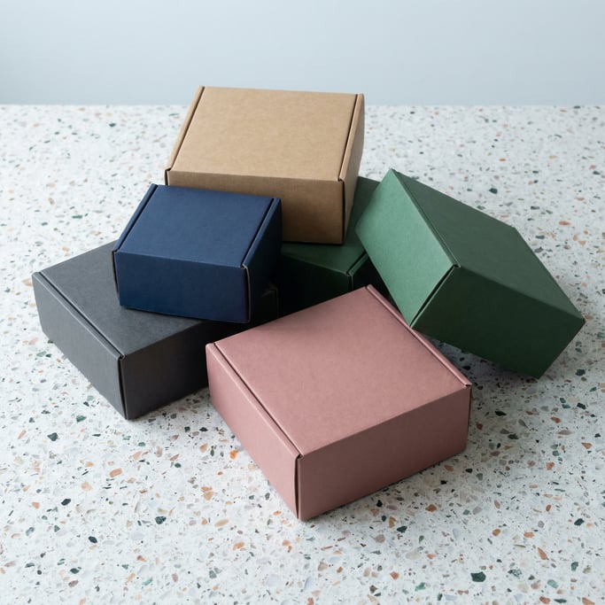 Kraft cardboard box, scattered arrangement of five boxes, each a different color — kraft brown