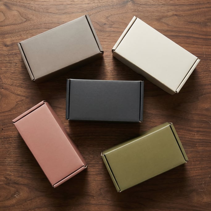 Tuck-end box, scattered arrangement of five boxes, each a different color — matte warm grey