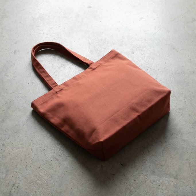 Canvas tote bag in matte rust, lying on its side