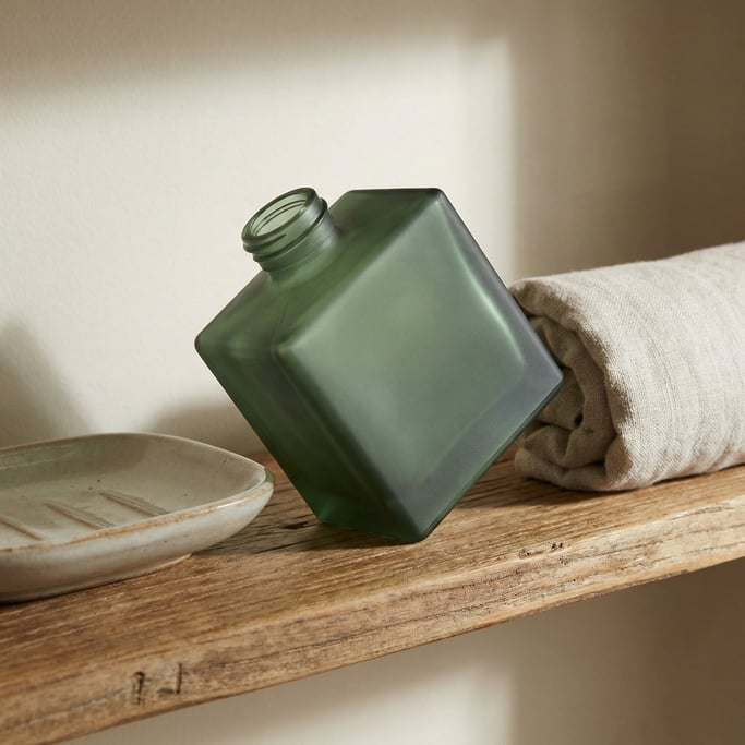 Square glass bottle in matte forest green, single at dramatic angle
