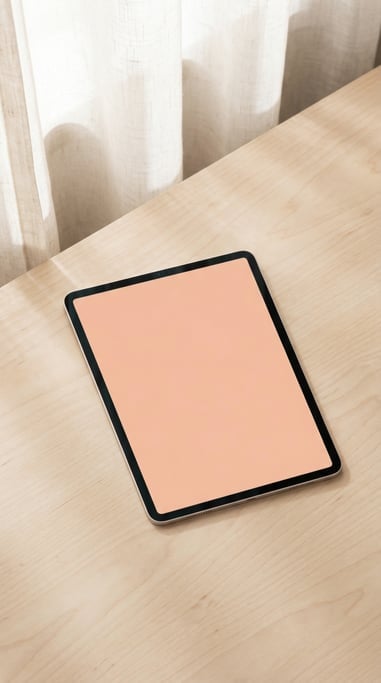 Tablet face up on a light birch desk, blank solid soft peach screen with no content