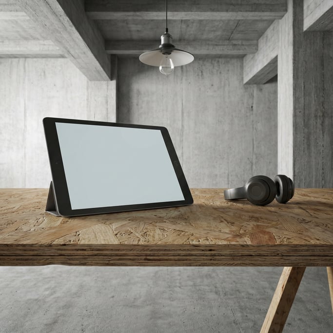 Slim tablet on a raw plywood desk, blank solid light grey screen with no content or UI