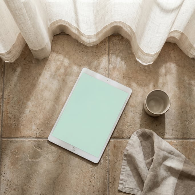 Tablet lying flat on a ceramic tile surface, blank solid pale mint screen with no content