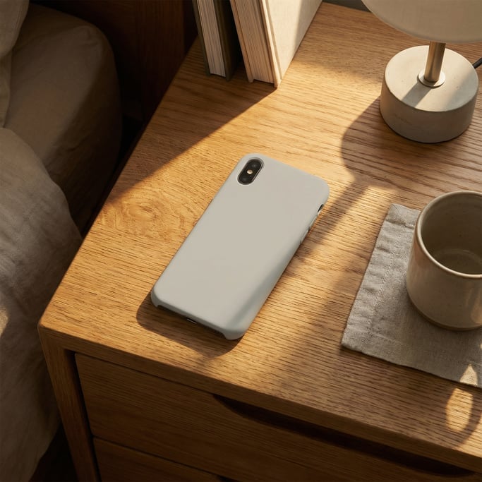 Smartphone face down showing back on a nightstand, blank solid pale grey screen with no content