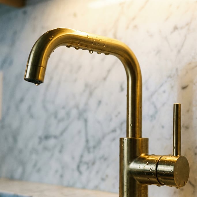 Close-up of a kitchen faucet in brushed brass with water droplets on the spout