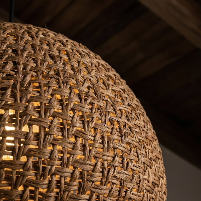 Detail of a woven rattan pendant light shade showing the tight weave pattern and the warm glow of th