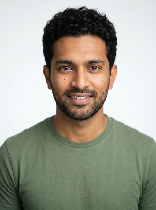Professional studio headshot of a 27-year-old South Asian man with short curly black hair