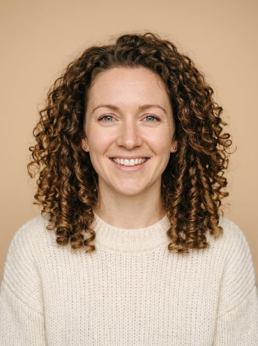 Professional studio headshot of a 32-year-old White British woman with shoulder-length coily natural