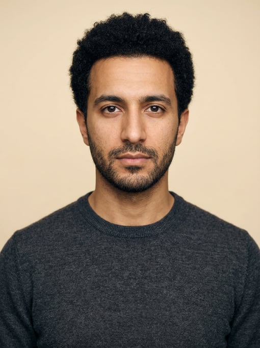 Professional studio headshot of a 29-year-old Turkish man with a short natural afro in black