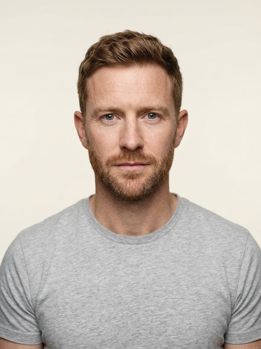 Professional studio headshot of a 36-year-old White British man with short red-brown hair