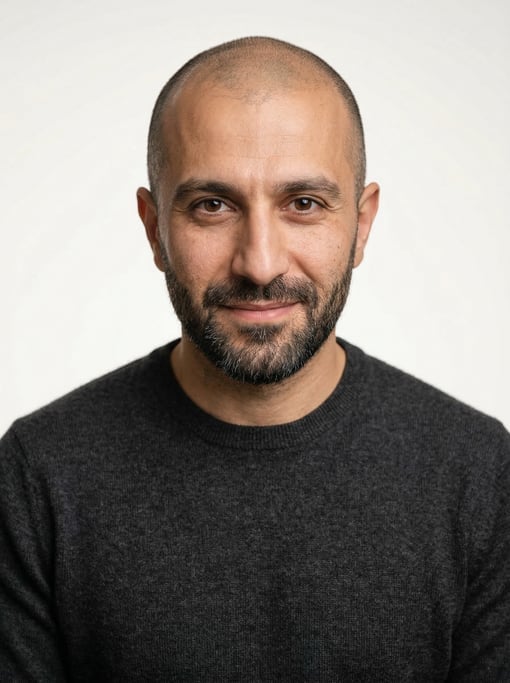 Professional studio headshot of a 33-year-old Persian man with a shaved head