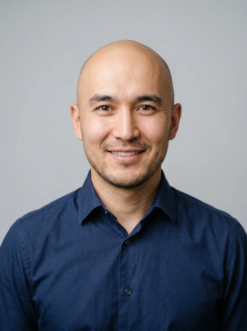 Professional studio headshot of a 32-year-old Central Asian man with a completely bald head