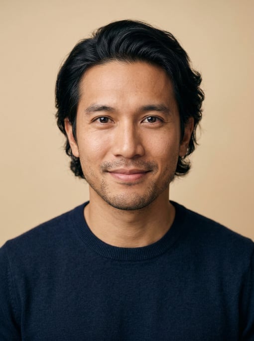 Professional studio headshot of a 32-year-old Southeast Asian man with medium-length wavy black hair