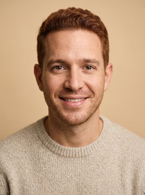 Professional studio headshot of a 36-year-old Cuban man with short auburn hair