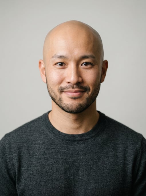 Professional studio headshot of a 28-year-old Japanese man with a completely bald head