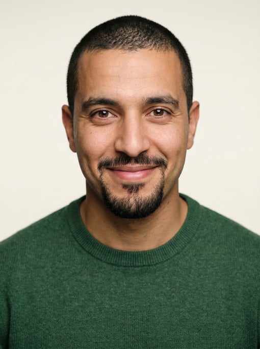 Professional studio headshot of a 29-year-old North African man with a buzz cut in black, a goatee