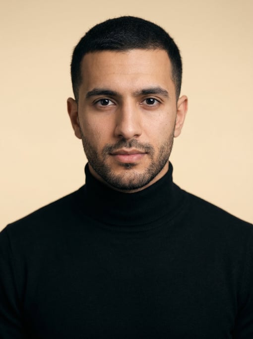 Professional studio headshot of a 27-year-old Middle Eastern man with short cropped black hair