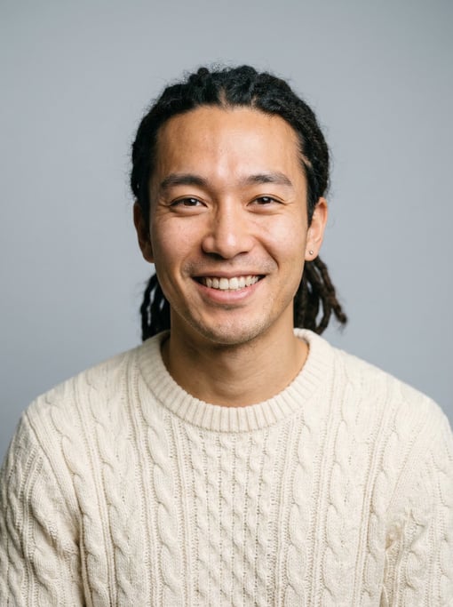 Professional studio headshot of a 26-year-old Japanese man with medium dreadlocks pulled back