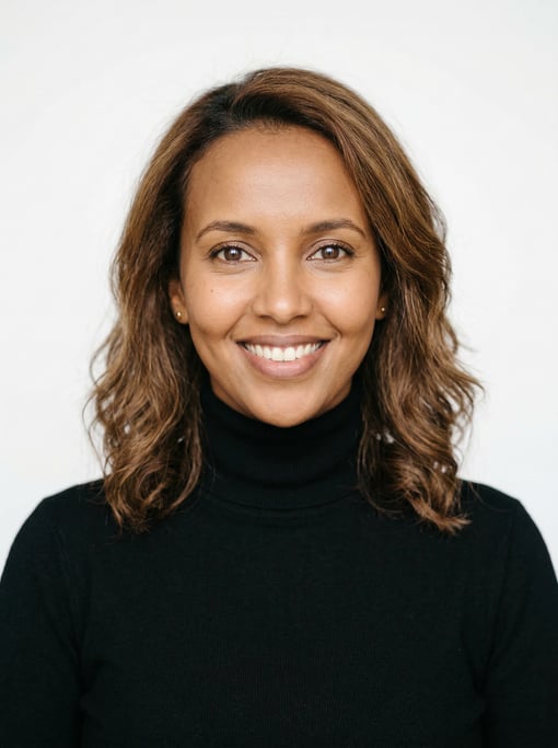 Professional studio headshot of a 32-year-old Somali woman with shoulder-length wavy chestnut hair