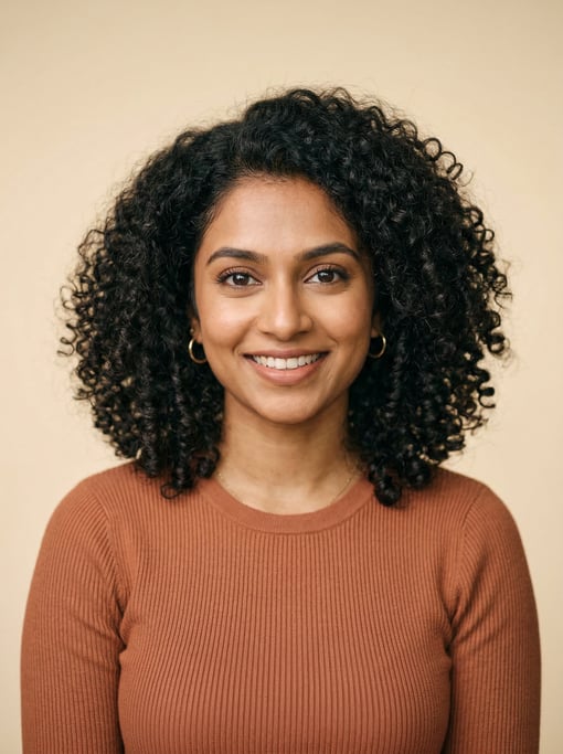 Professional studio headshot of a 25-year-old South Asian woman with shoulder-length coily natural h