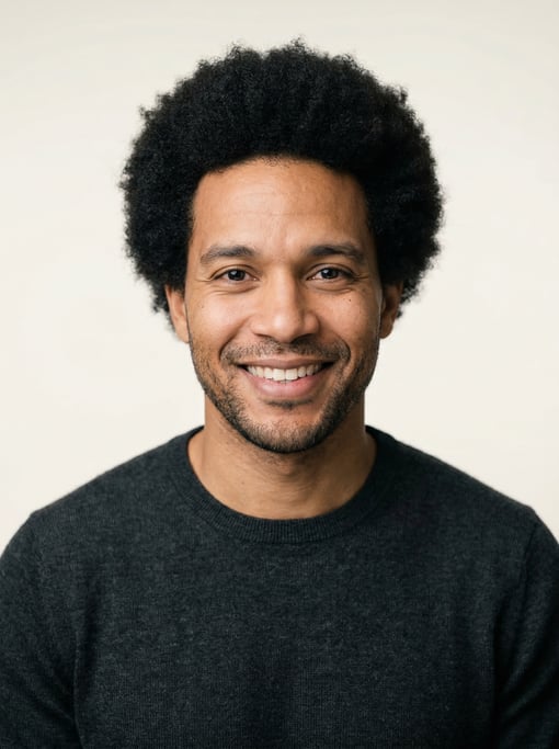 Professional studio headshot of a 36-year-old mixed-race man with a medium natural afro in black