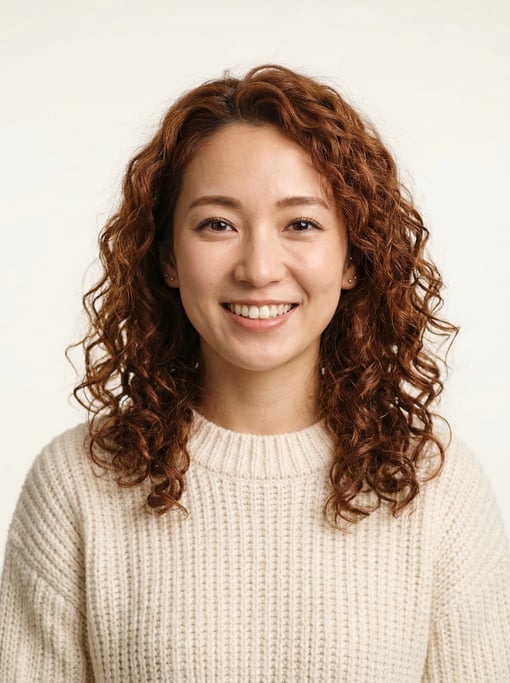 Professional studio headshot of a 26-year-old Japanese woman with shoulder-length curly auburn hair