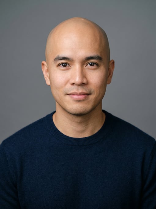 Professional studio headshot of a 33-year-old Southeast Asian man with a completely bald head