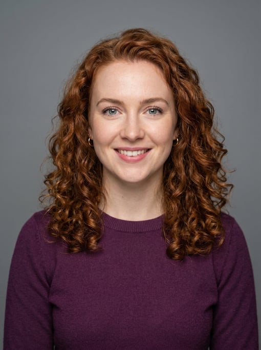 Professional studio headshot of a 26-year-old White British woman with shoulder-length curly auburn