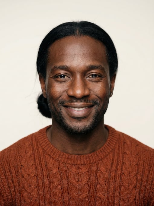 Professional studio headshot of a 33-year-old West African man with long straight black hair tied ba