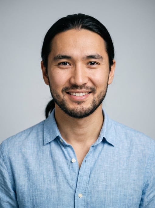 Professional studio headshot of a 26-year-old Central Asian man with long straight black hair tied b