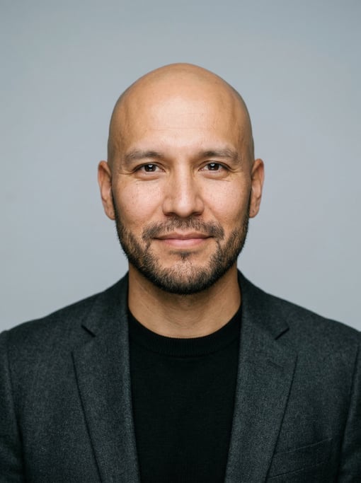 Professional studio headshot of a 35-year-old Native American man with a completely bald head