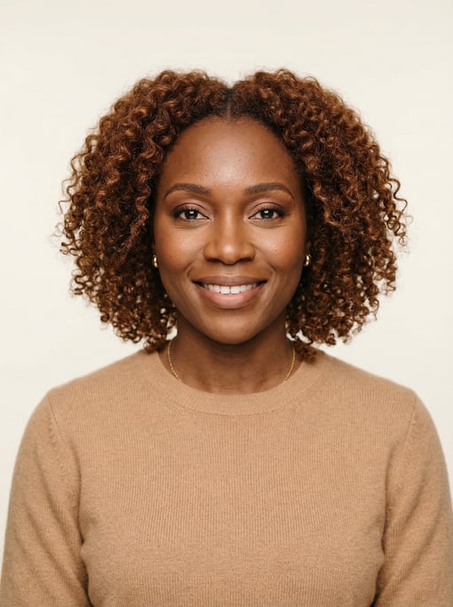Professional studio headshot of a 35-year-old West African woman with shoulder-length curly auburn h
