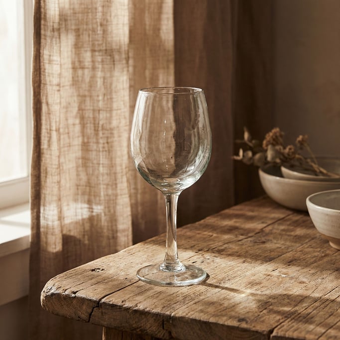 A wine glass catching light on a wooden table, warm tones, no wine, just the glass form