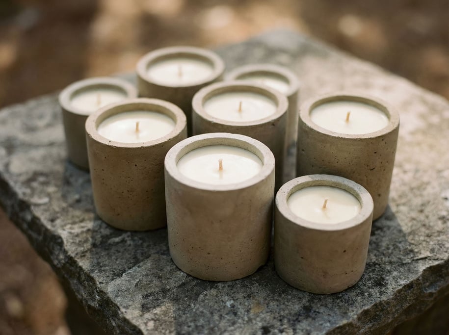 Hand-poured candles in raw concrete vessels, arranged asymmetrically on a stone surface (guq5tbur)