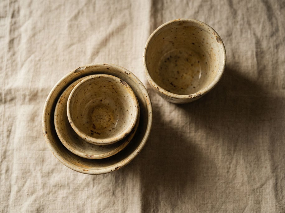 Three speckled ceramic cups in graduating sizes, nested together, overhead on a linen cloth (jlltjt)