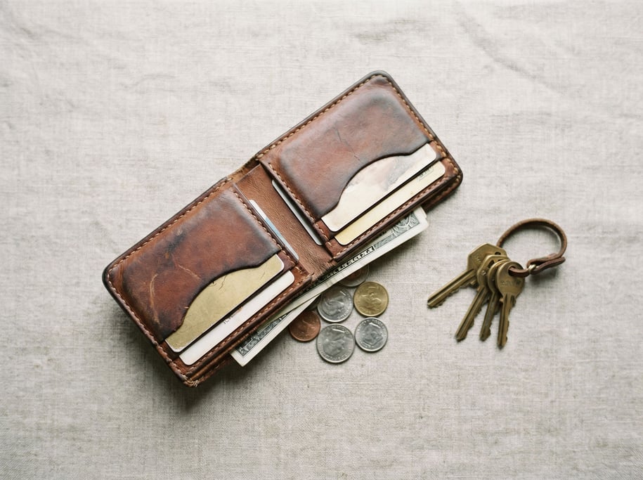 A hand-stitched leather wallet, aged to a rich patina, contents spilling slightly, keys beside it (km0l3ol)