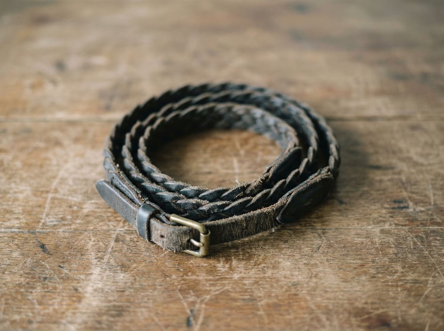 A vintage camera strap coiled on a wooden surface, braided leather showing years of neck wear (wfdufgym)