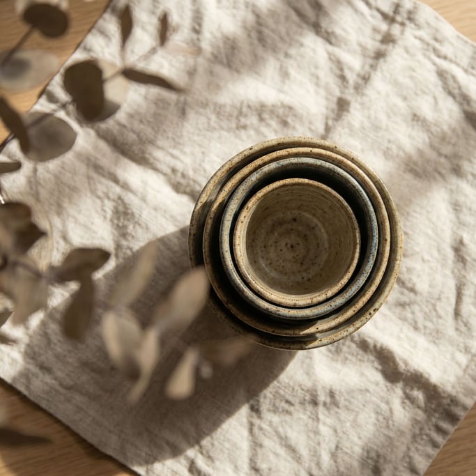 Three speckled ceramic cups in graduating sizes, nested together, overhead on a linen cloth