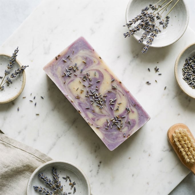 A bar of handmade soap in cool lavender tones, resting on a marble slab (fzfvdw5i)