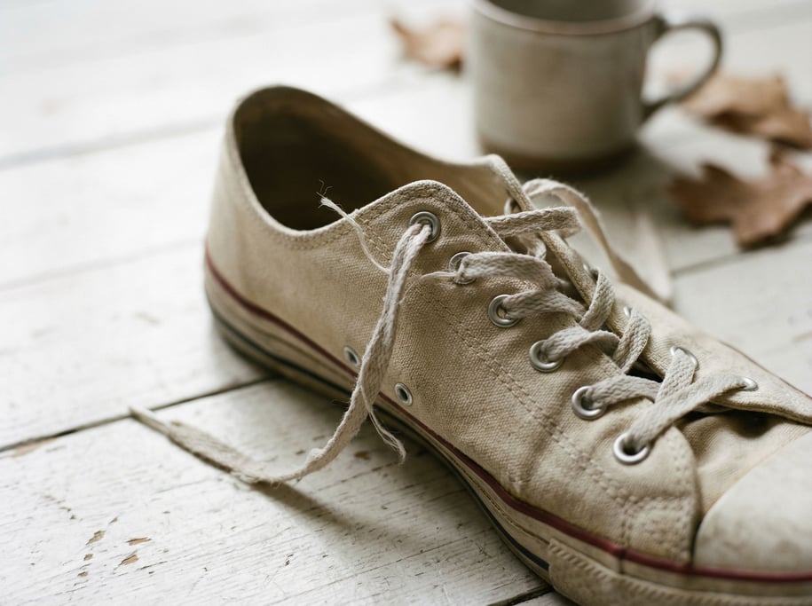A pair of raw canvas sneakers on a whitewashed wood floor, laces untied, casual and lived-in (ynnbcgy1)